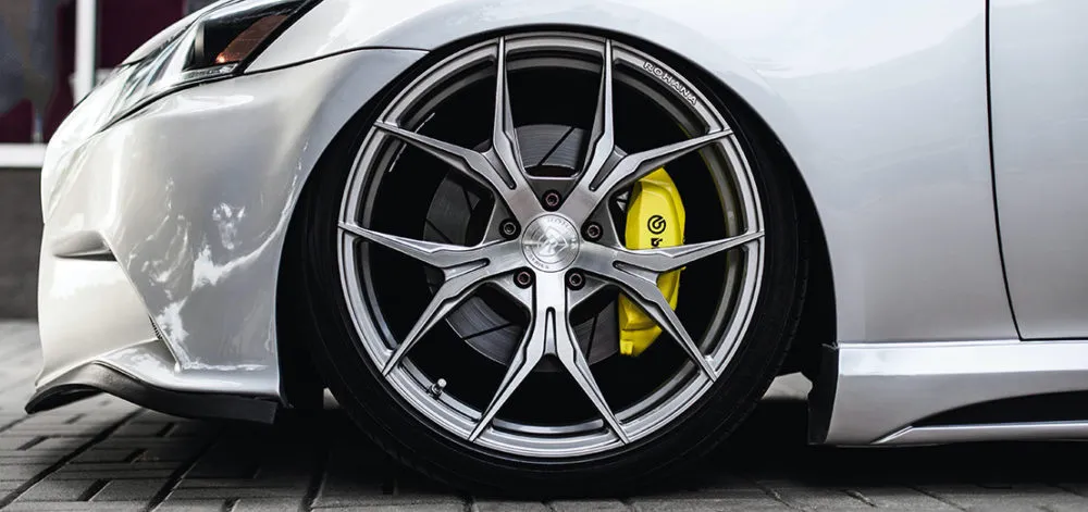 Close-up of a silver car’s front wheel with a low-profile tire, featuring a yellow Brembo brake caliper and multi-spoke alloy rim, showcasing the importance of personal insurance for high-performance vehicles.